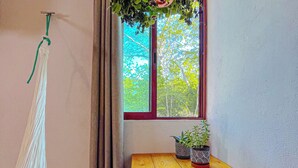 A room with a wooden table, a hanging plant, a hammock, and a window with curtains.