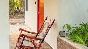 A wooden rocking chair and a bench outside a building with a red door and a small potted plant.