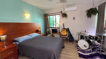 A bedroom with a bed, a desk, a guitar, a drum set, and a ceiling fan.