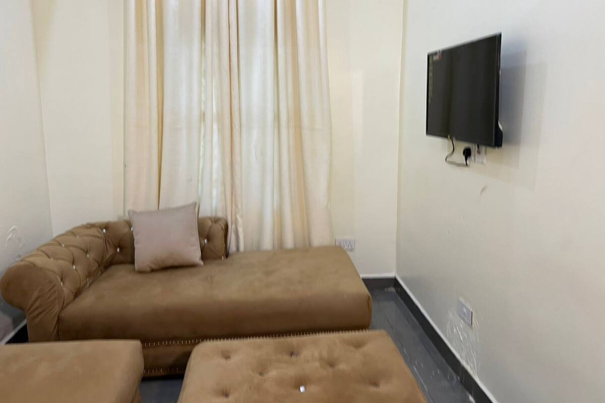 A room with a sofa bed, a flat-screen TV mounted on the wall, and a window with curtains.