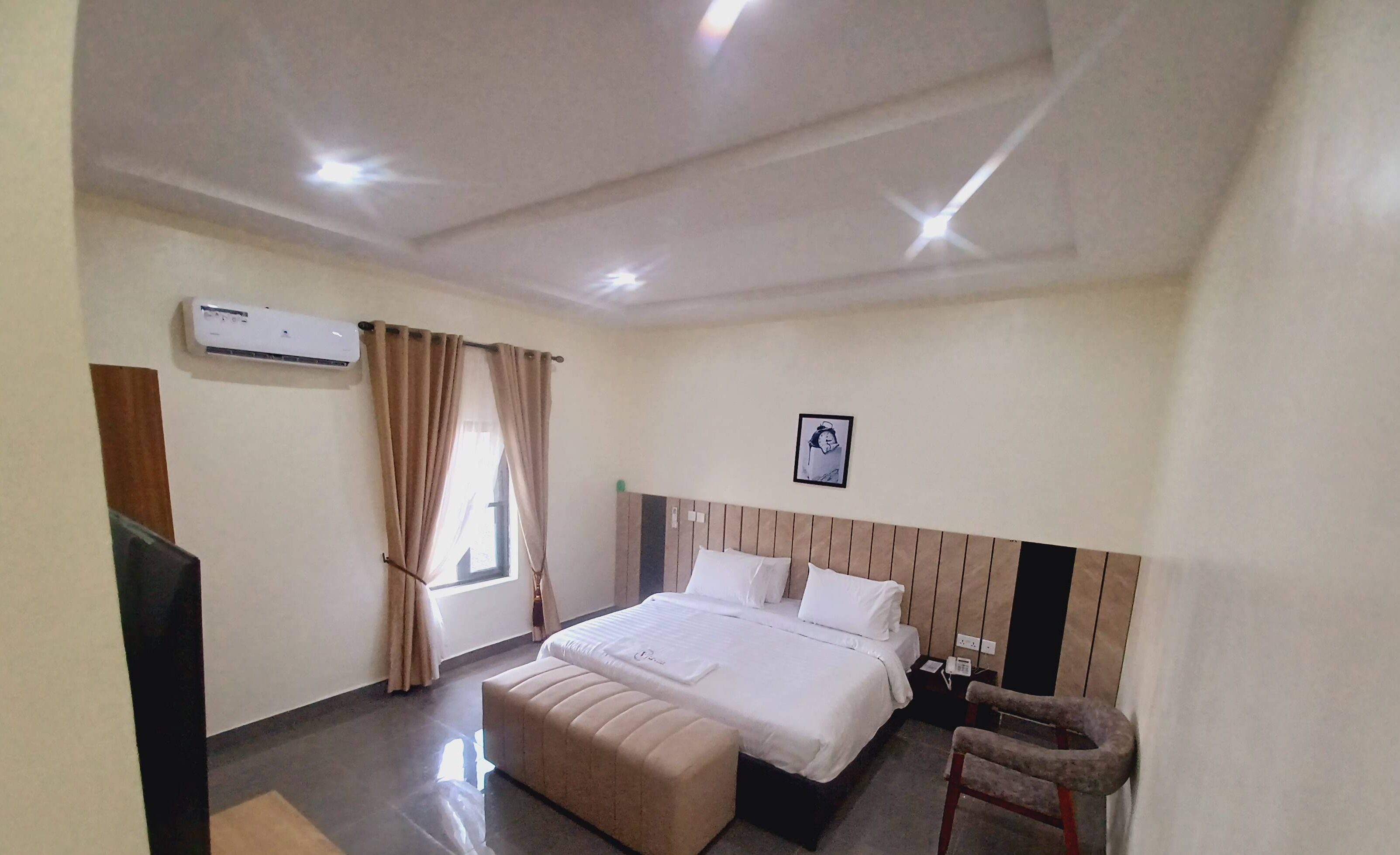 Ein Hotelzimmer mit Bett, Sessel, Schreibtisch, Klimaanlage und einem Vorhangfenster.