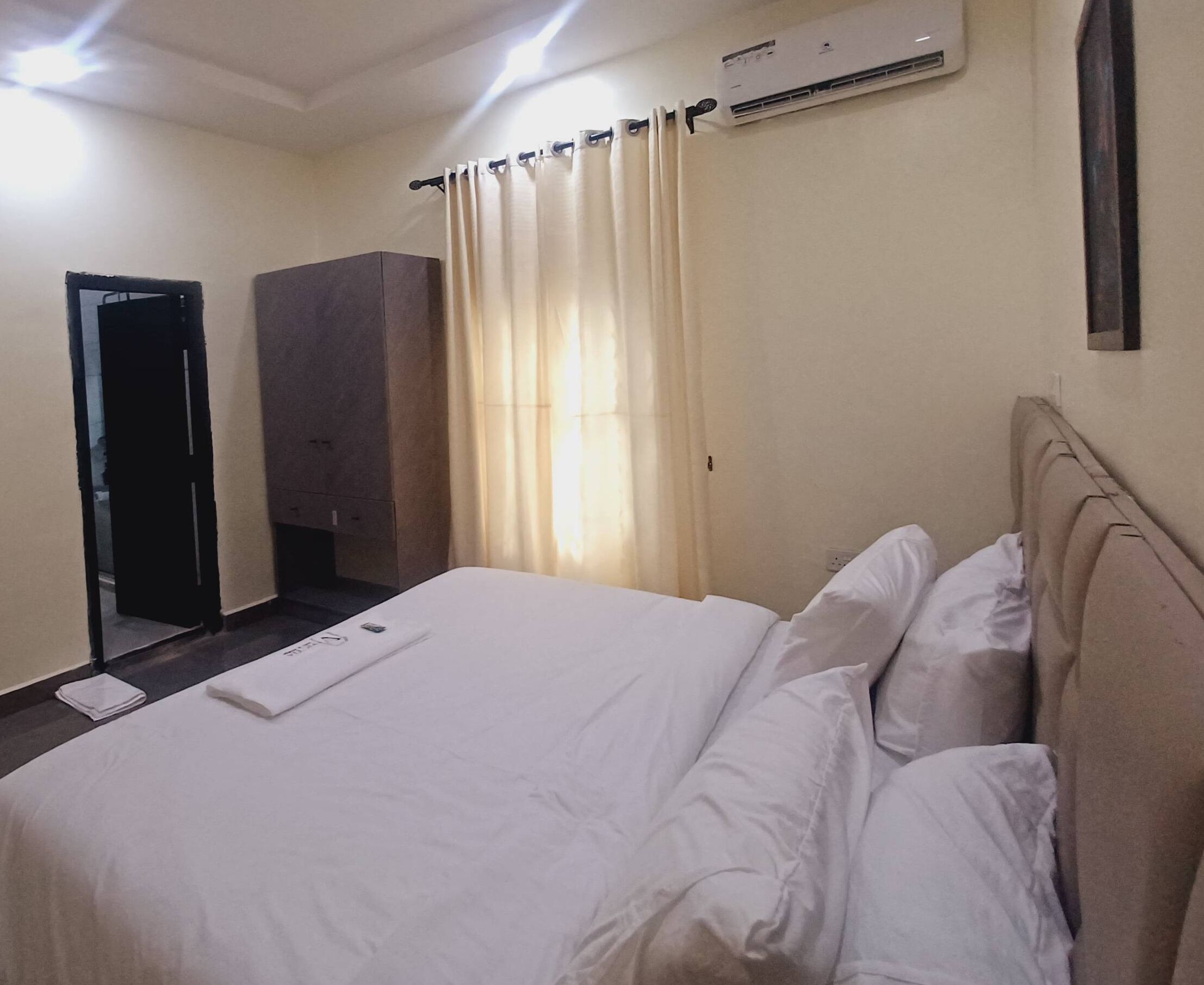 Una habitación de hotel con cama, cortinas, un equipo de aire acondicionado y un armario.
