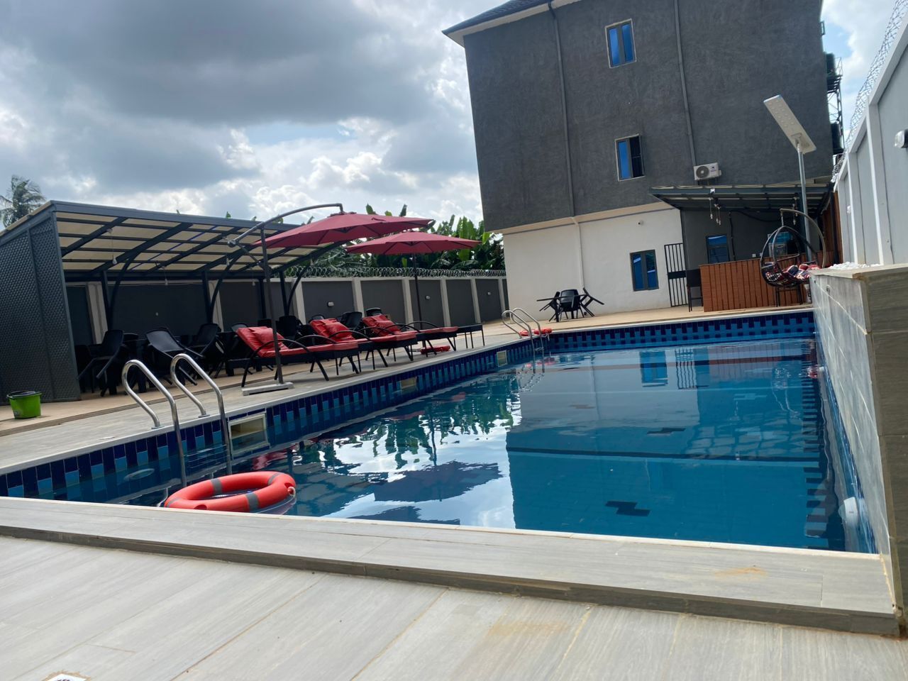 A swimming pool with lounge chairs and umbrellas, surrounded by a building with a covered patio.