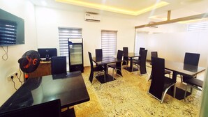 A conference room with a glass table, black chairs, a black refrigerator, and a flat-screen TV on the wall. - Victia Suite and Lounge (Ijebu Ode)