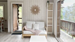 A cozy room with a wooden floor, a white sofa, a white coffee table, and a large window offering a view of the outdoors. - Cocooning cottage in the heart of nature (Saxon)