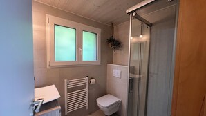 A bathroom with a toilet, a glass shower enclosure, a towel rack, and a window with frosted glass. - Cocooning cottage in the heart of nature (Saxon)