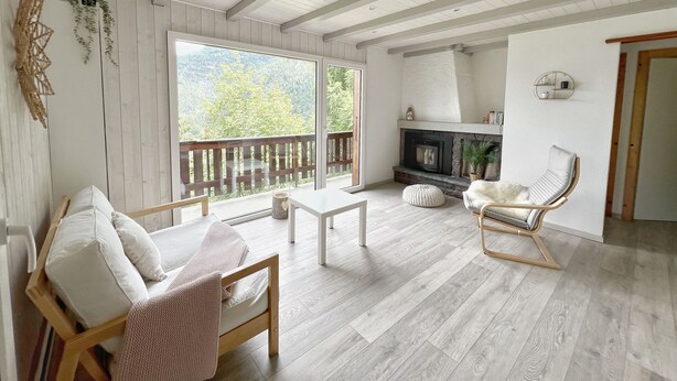 A spacious living area with a fireplace, wooden flooring, and a balcony with a view of greenery. - Cocooning cottage in the heart of nature (Saxon)