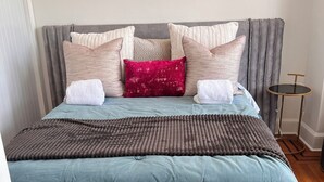 Una cama con cabecera gris, varios almohadones y una colcha azul.