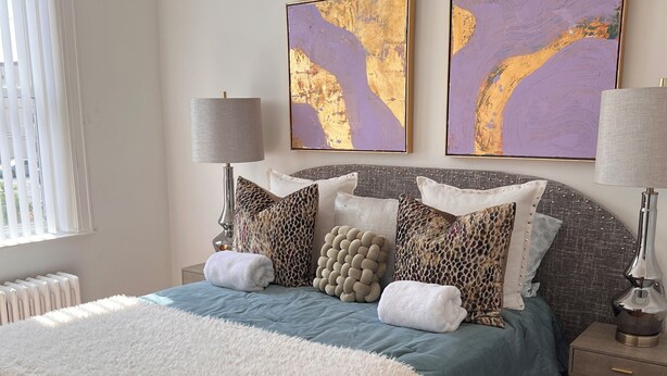 Un dormitorio con una cama grande, dos mesitas de noche, un radiador y dos cuadros abstractos en la pared.
