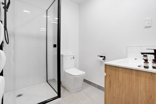 A modern bathroom with a glass shower enclosure, a white toilet, and a wooden vanity with toiletries.