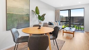 A modern living room with a round wooden table, two grey upholstered chairs, a sofa, and a large abstract painting on the wall.