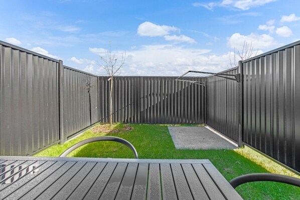 A fenced backyard with a wooden table and a hose.