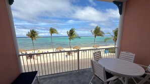 Un balcón con vista a una playa, palmeras y cielo despejado.
