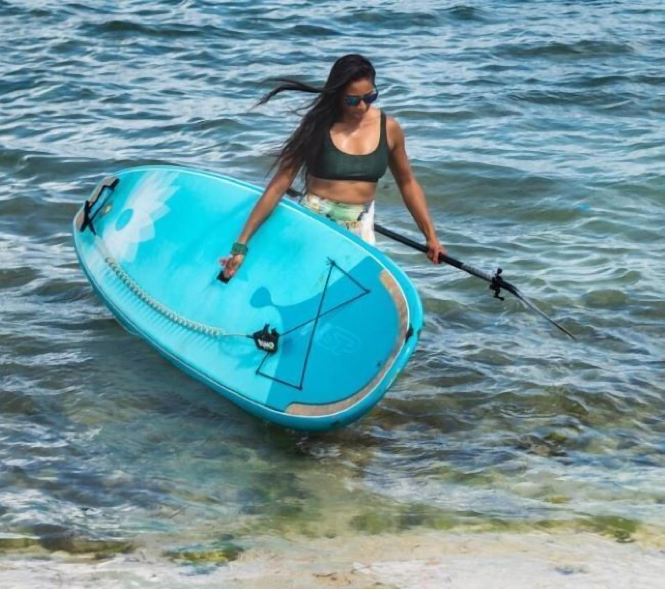 A person carrying a blue paddleboard.