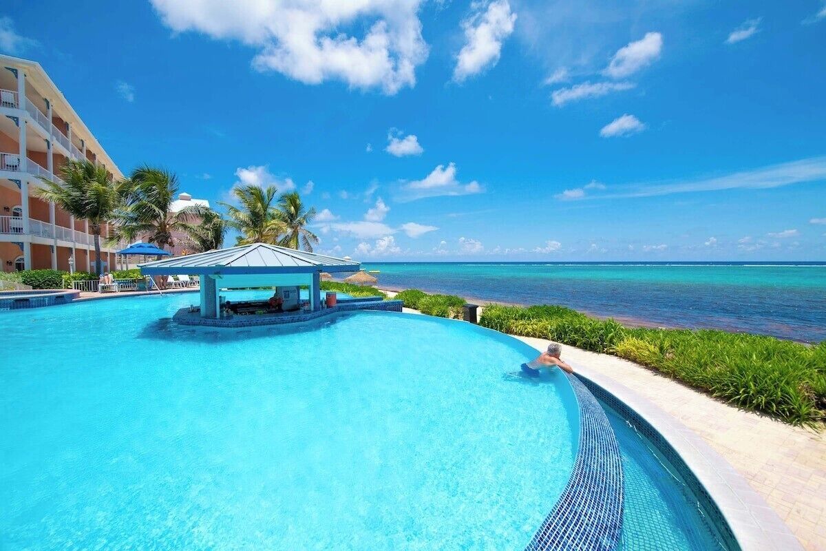 A resort pool with a cabana, palm trees, and a view of the ocean.