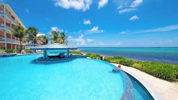 A resort pool with a cabana, palm trees, and a view of the ocean.
