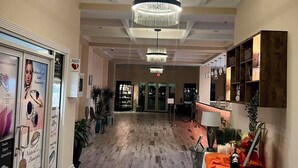Un vestíbulo de hotel con piso de madera, un candelabro, un mostrador de recepción y una mesa con una botella y vasos.