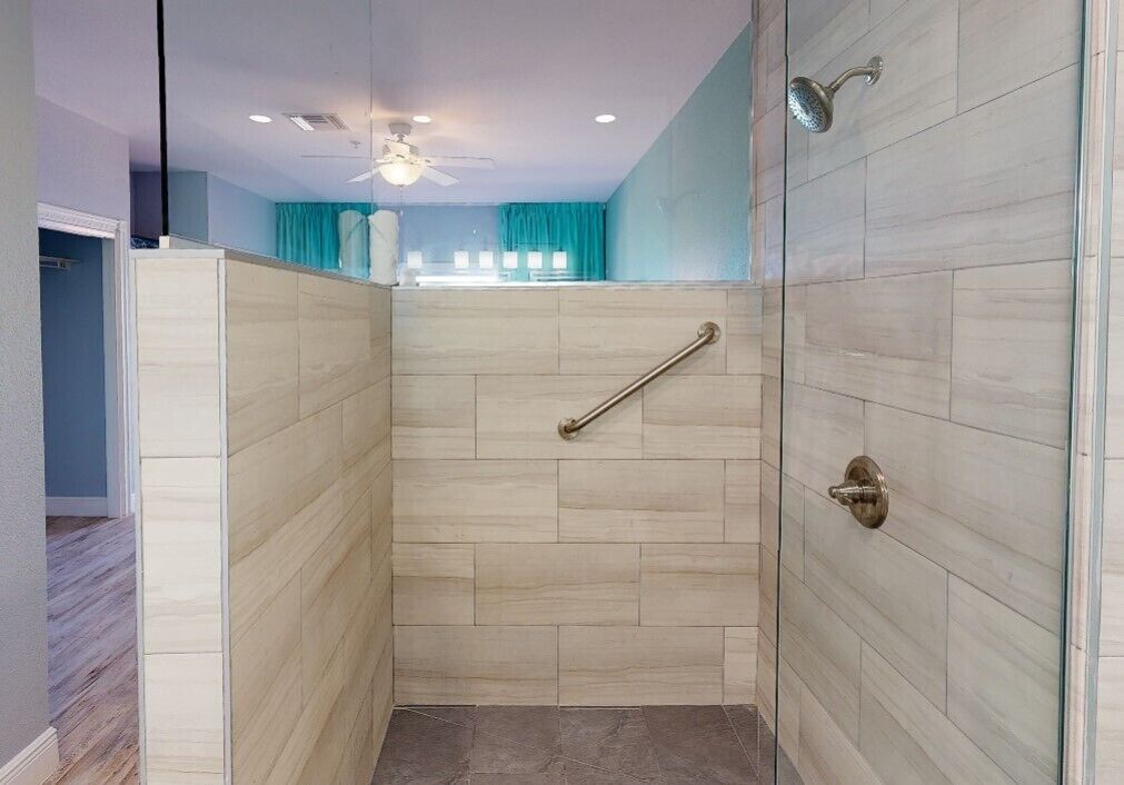 A walk-in shower with a glass door, a handrail, and a ceiling fan.
