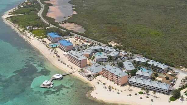 Vista aérea de un resort con varias edificaciones, una playa y aguas cristalinas.