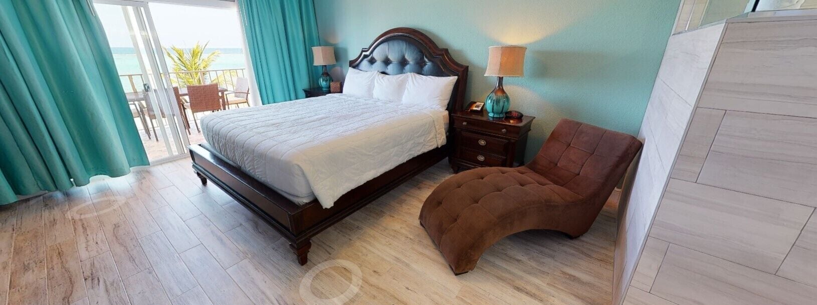 A bedroom with a bed, a nightstand, a chair, and a view of the outdoors.