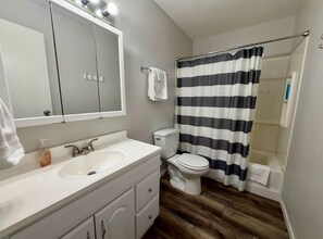 A bathroom with a white sink, a mirror, a toilet, and a shower curtain. - Great North Lodging (Anchorage)