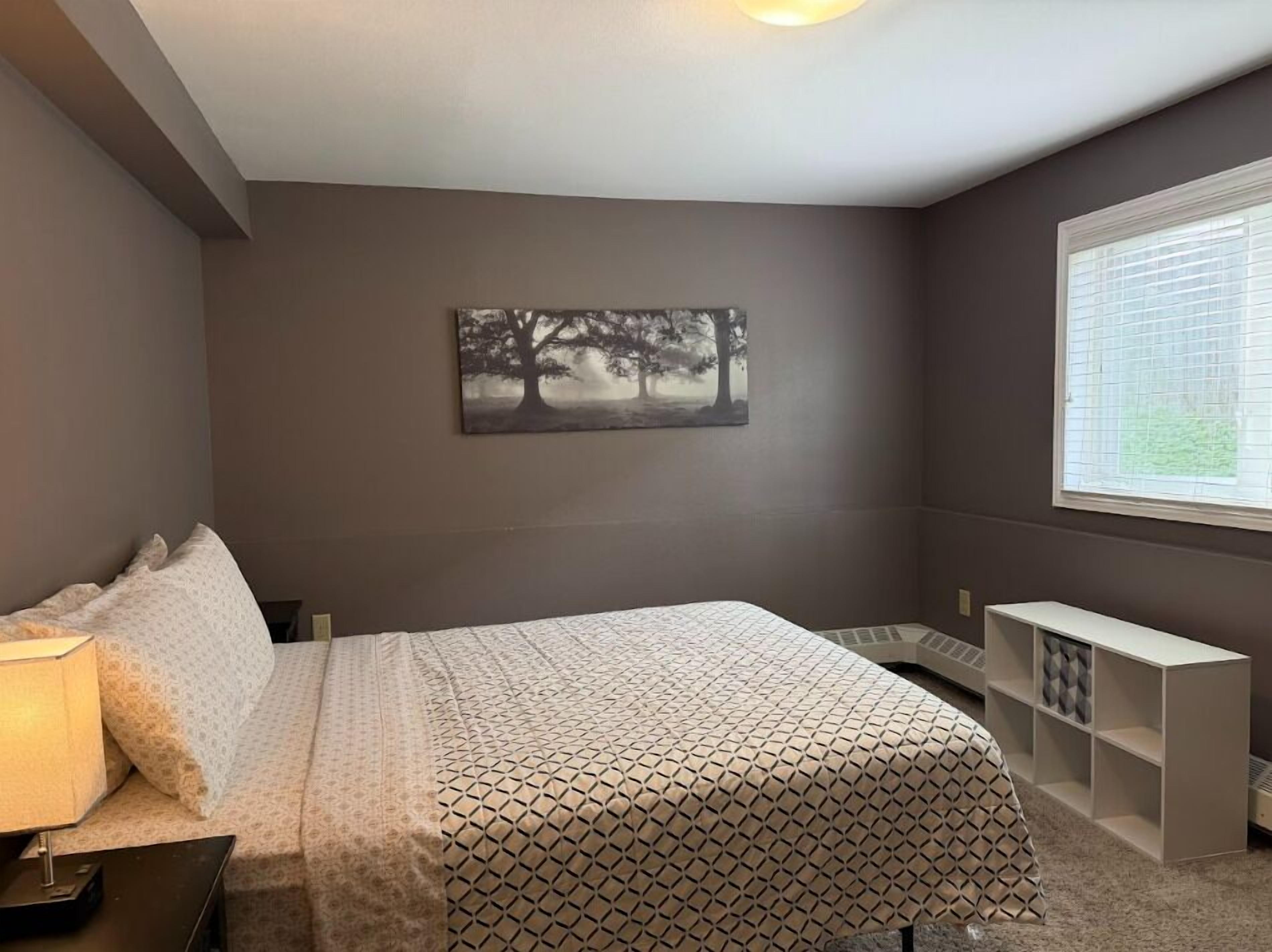 Een slaapkamer met een bed, nachtkastje, lamp en een raam met jaloezieën.