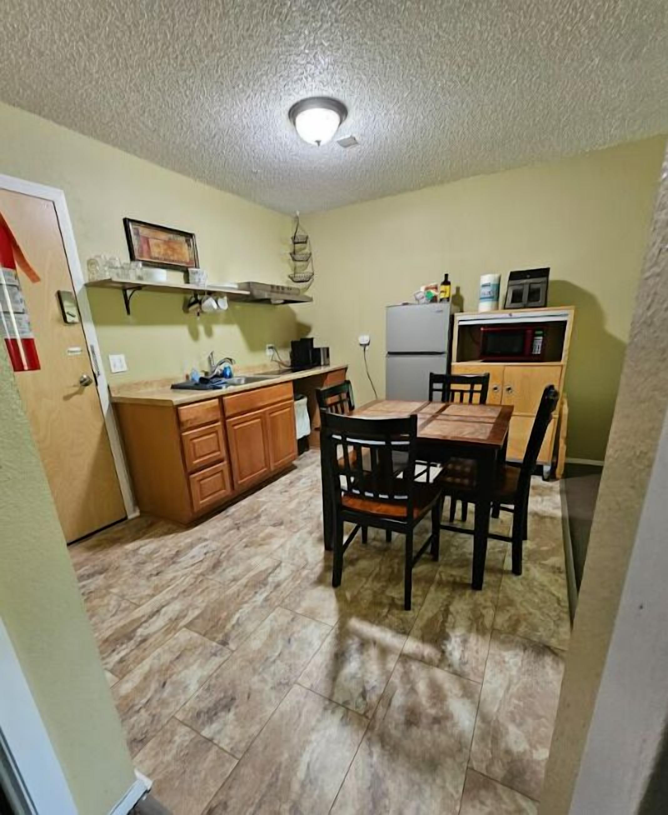 A compact kitchen with a dining table and chairs, a microwave, and a refrigerator.