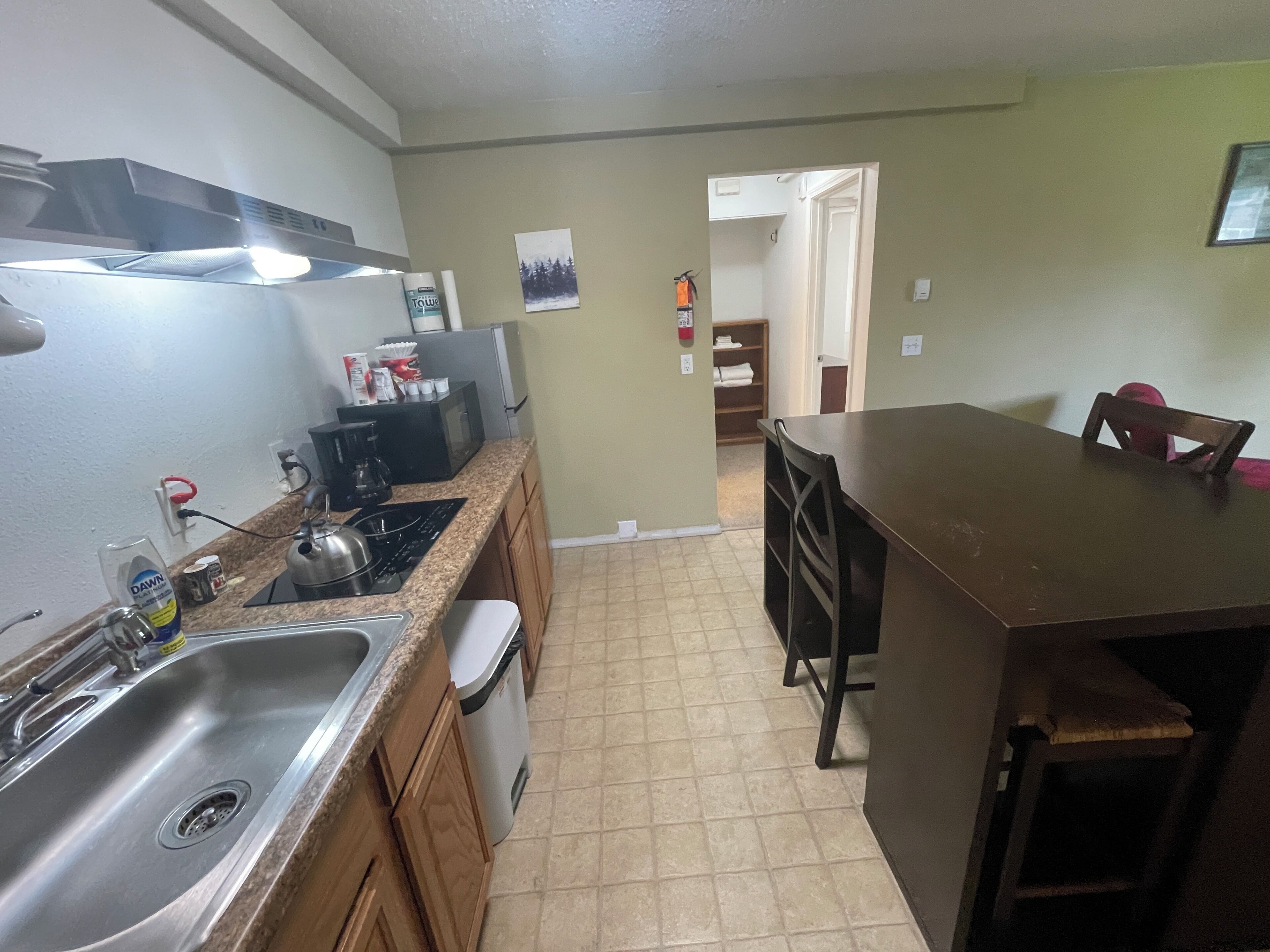 A kitchen with a sink, stove, and cabinets. There is a dining area with a table and chairs.
