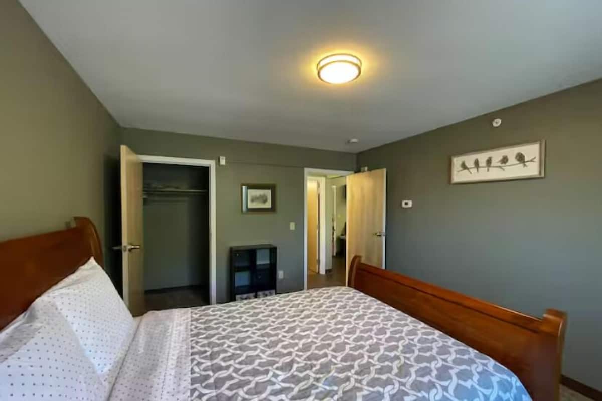 A bedroom with a bed, a wardrobe, a desk, and a framed picture on the wall.
