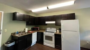 A compact kitchen with dark cabinets, a white stove, and a refrigerator. - Great North Lodging (Anchorage)