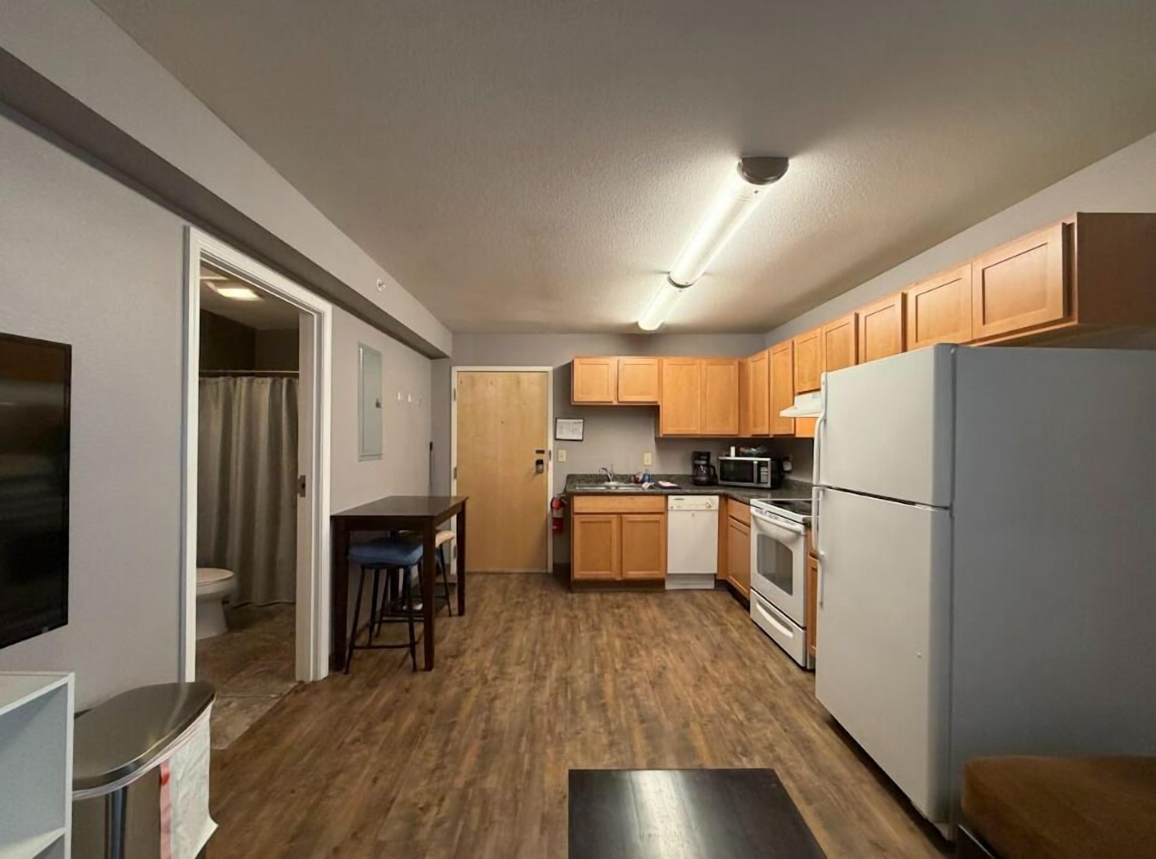 A compact kitchen with wooden cabinets, a microwave, a refrigerator, and a dining area with a table and chairs.