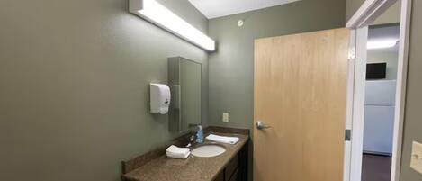 A bathroom with a granite countertop, a mirror, a hand dryer, and a wooden door.