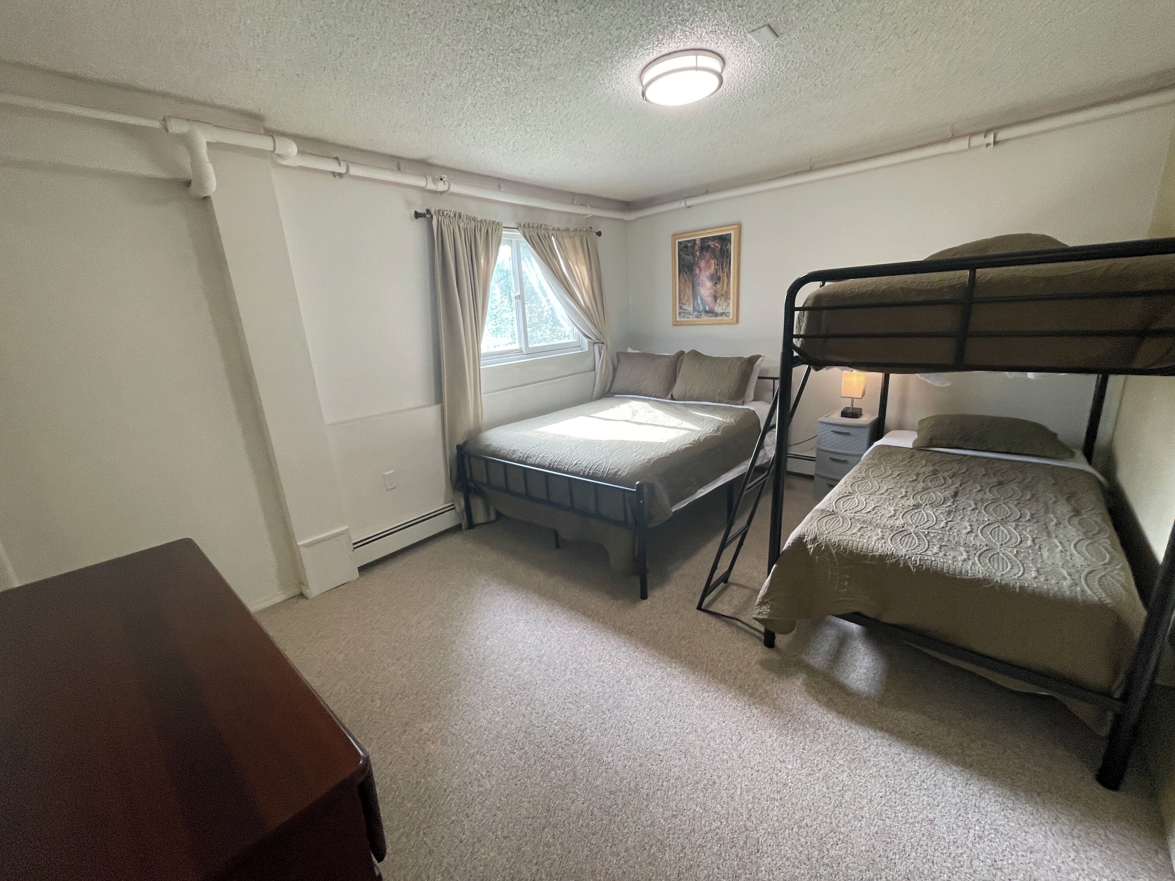 Una habitación con literas, una cama individual, una mesita y una ventana con cortinas.