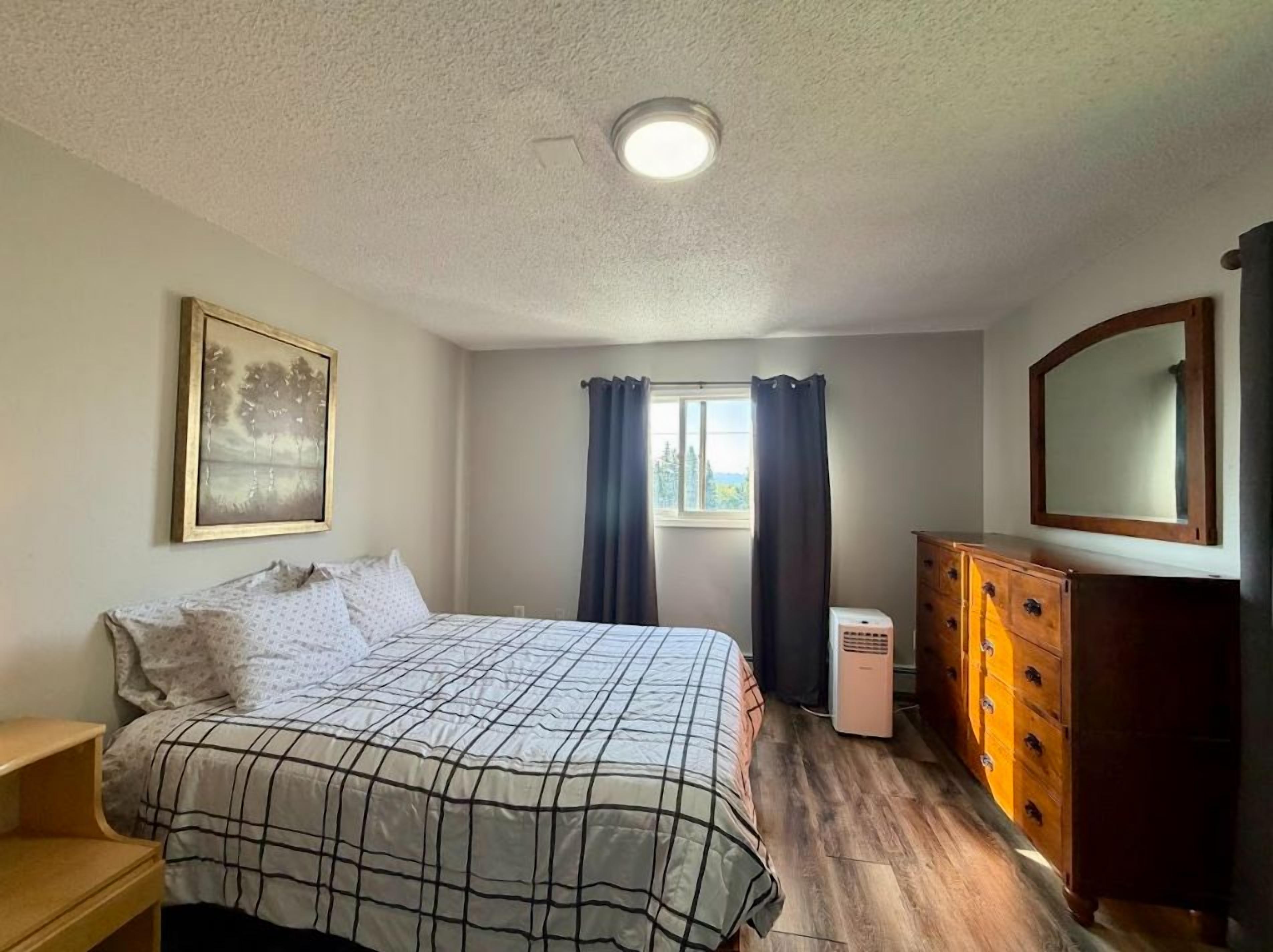 A bedroom with a bed, a dresser, a mirror, and a window with curtains.