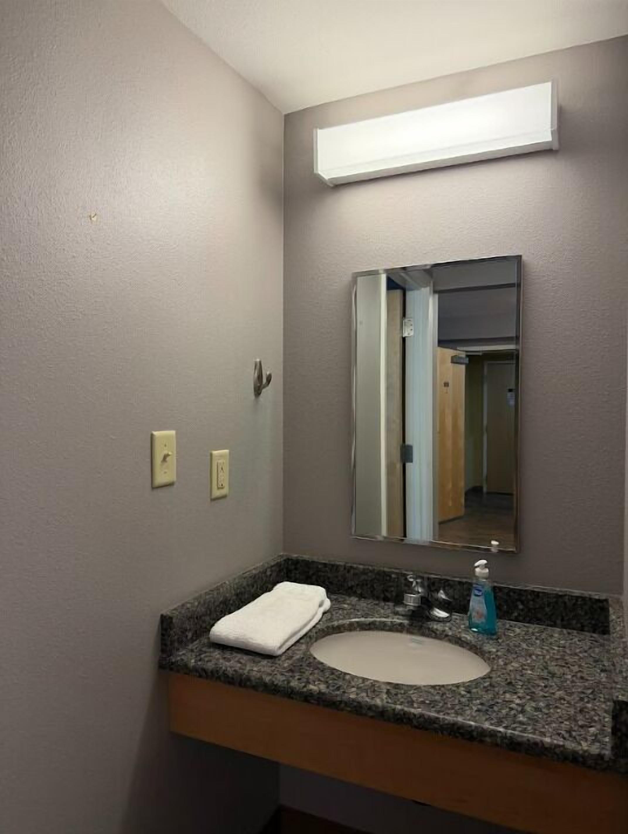 Un baño con encimera de granito, un lavabo, un espejo y una toalla.