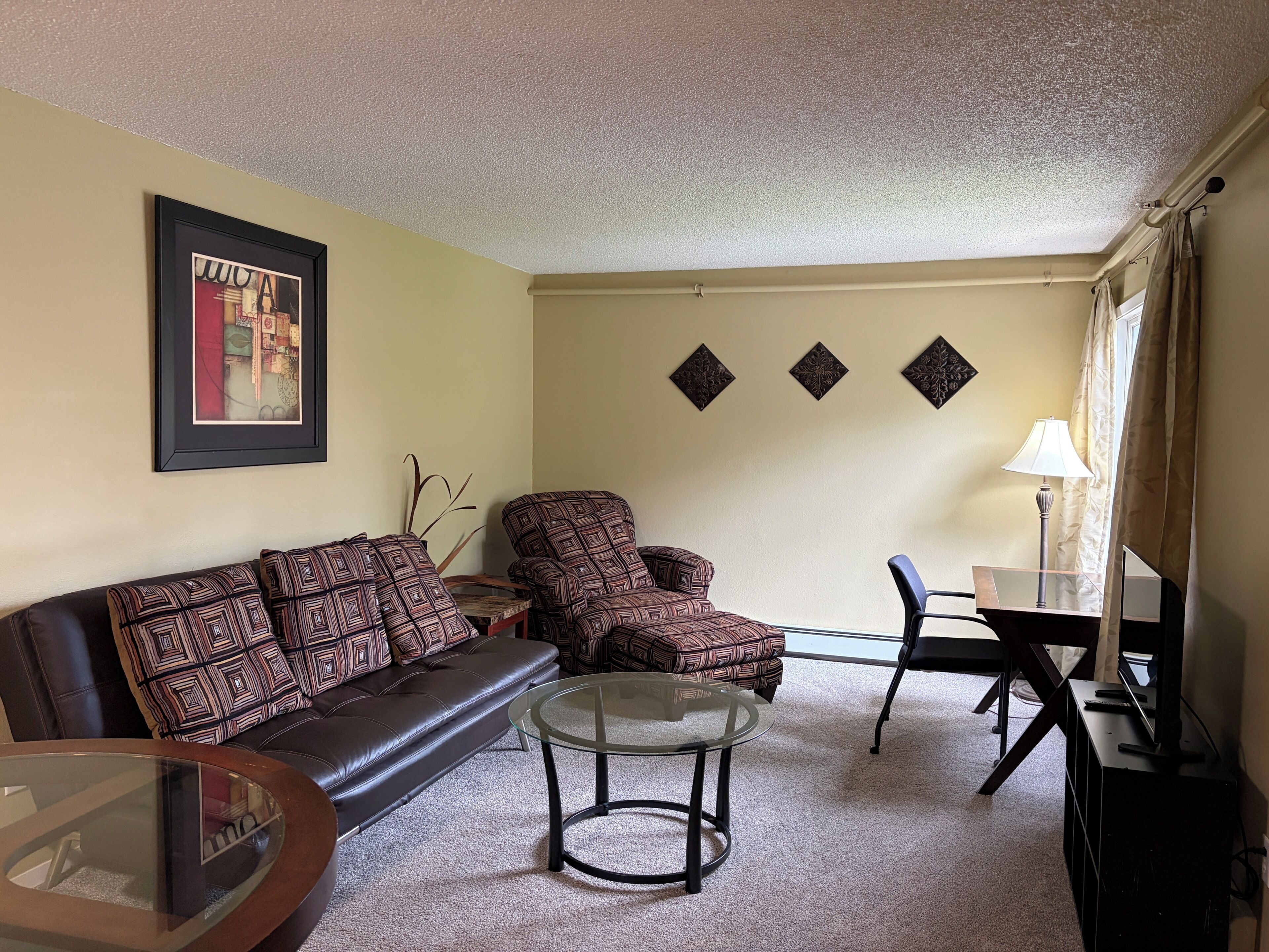 A living room with a sofa, armchair, glass coffee table, and a TV stand.