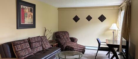 A living room with a sofa, armchair, glass coffee table, and a TV stand.
