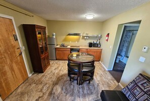 A compact kitchen with a dining table, wooden cabinets, and a microwave. - Great North Lodging (Anchorage)