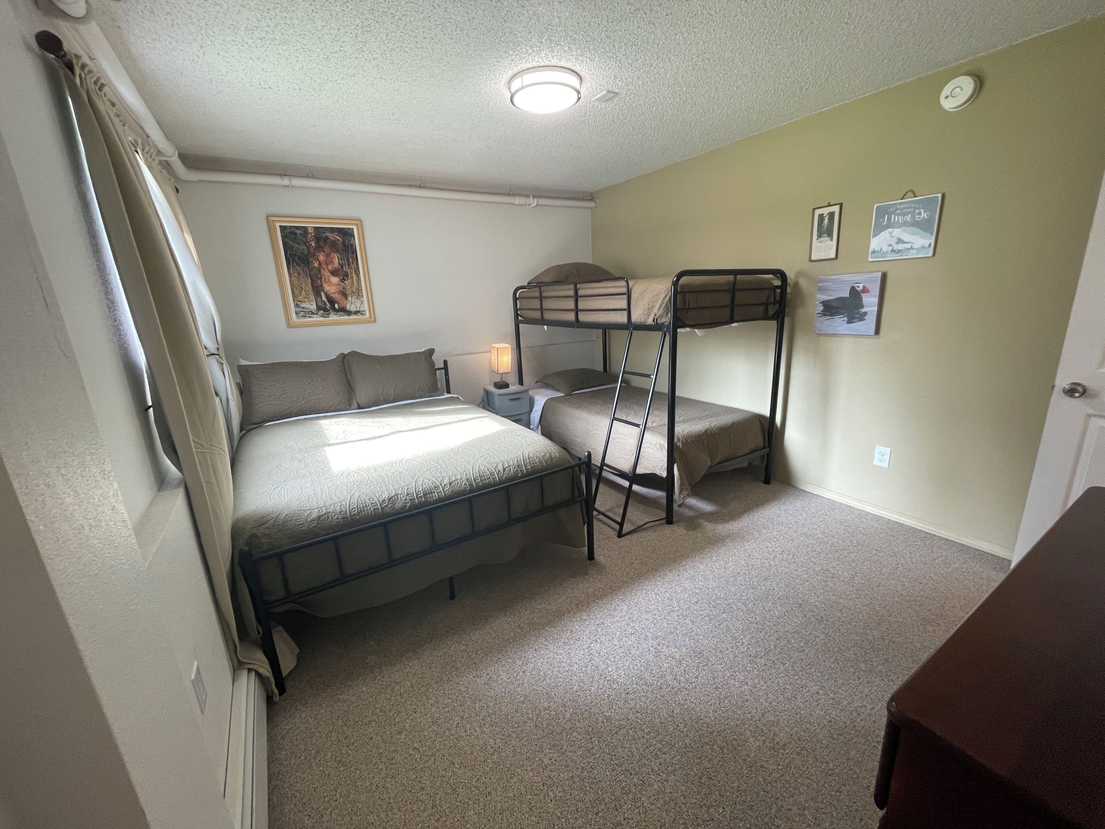 A room with bunk beds, a bedside table with a lamp, and a framed picture on the wall.