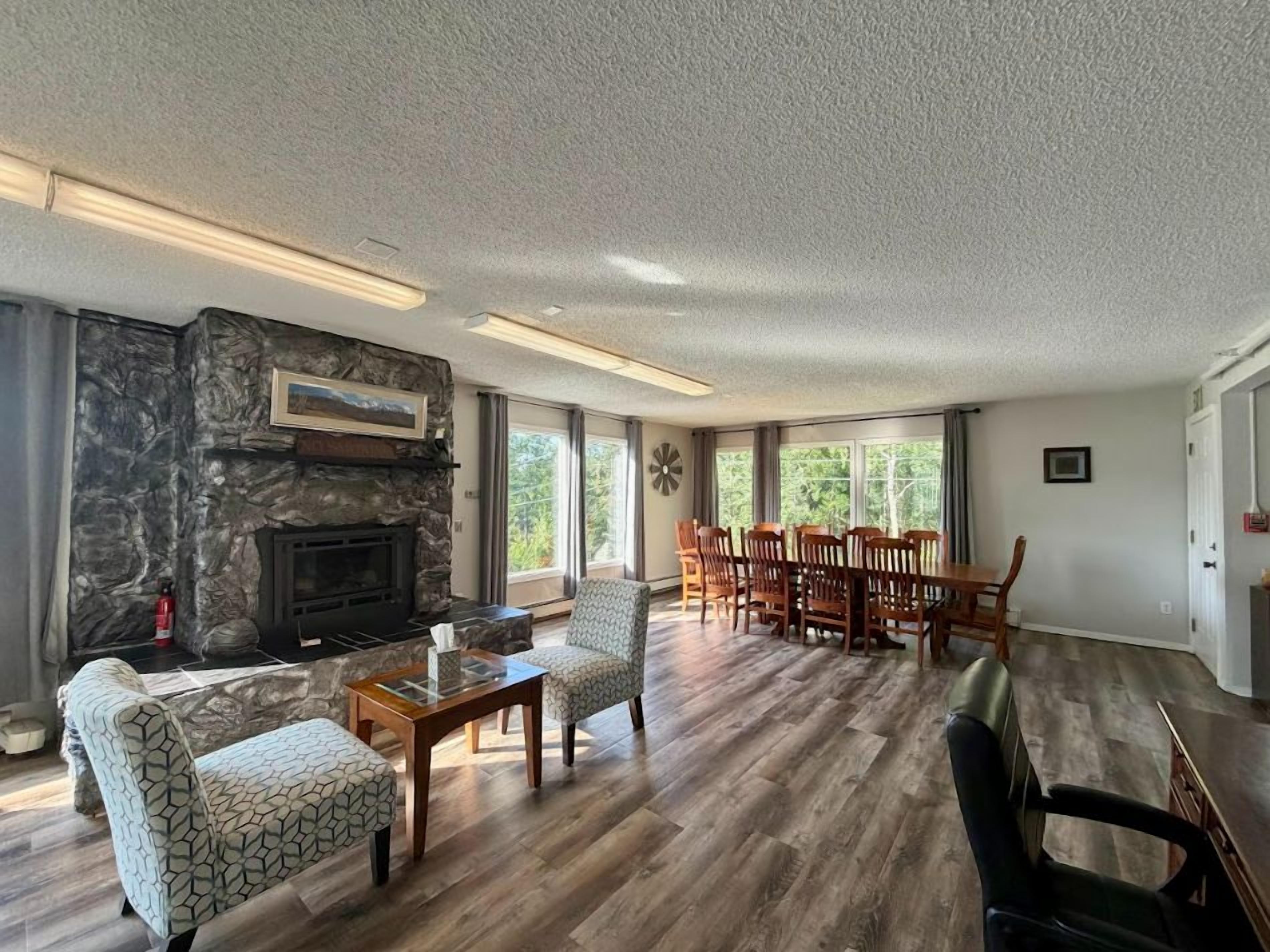 A spacious living room with a stone fireplace, wooden flooring, and a dining area with chairs and a table.