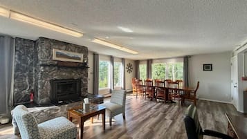 A spacious living room with a stone fireplace, wooden flooring, and a dining area with chairs and a table.