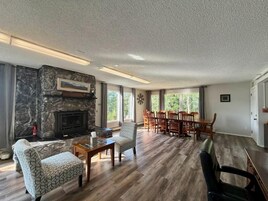 Uma sala de estar ampla com lareira de pedra, piso de madeira e área de jantar com cadeiras e mesa.