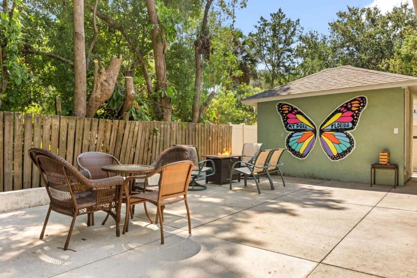 Un patio con mobiliario de mimbre, un mural de mariposas y una cerca de madera.