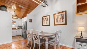Un comedor con una mesa y sillas de madera, una cocina al fondo y cuadros en la pared.