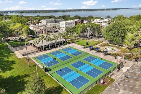 A tennis court complex with multiple courts, surrounded by greenery and buildings.
