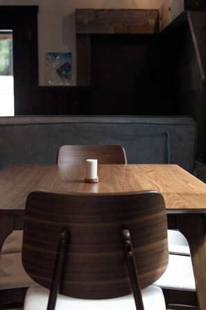 A wooden dining table with a white candle, a grey cushioned bench, and a wooden chair with a curved backrest. - Oz Lodge: Alice Chalet -Brand new, Alaskan chic chalet! (Seward)