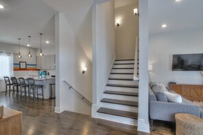 A spacious living area with a staircase, a kitchen with bar stools, and a flat-screen TV mounted on the wall. - HOWDY HOUSE-MUSIC CITY NASHVILLE (Nashville)