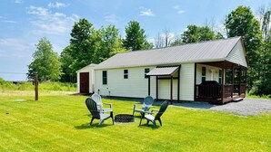 A house with a porch, a grassy yard, and two Adirondack chairs. - Sandy Pond Cozy Getaway (Pulaski)