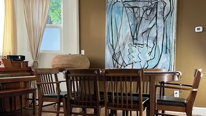 A dining area with a piano, wooden chairs, and a large abstract painting on the wall.