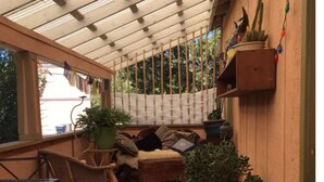 A covered porch with wooden flooring, a cushioned seating area, and potted plants.